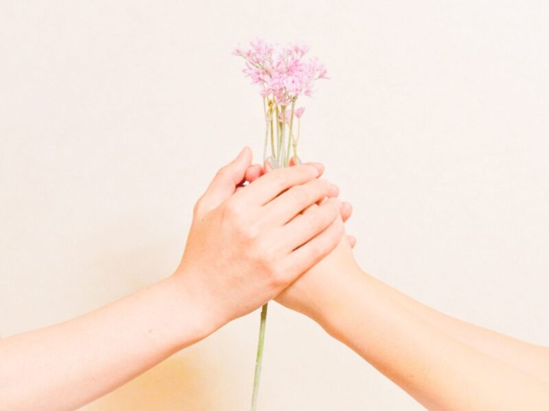 ピンク色の小花を握る2人の手